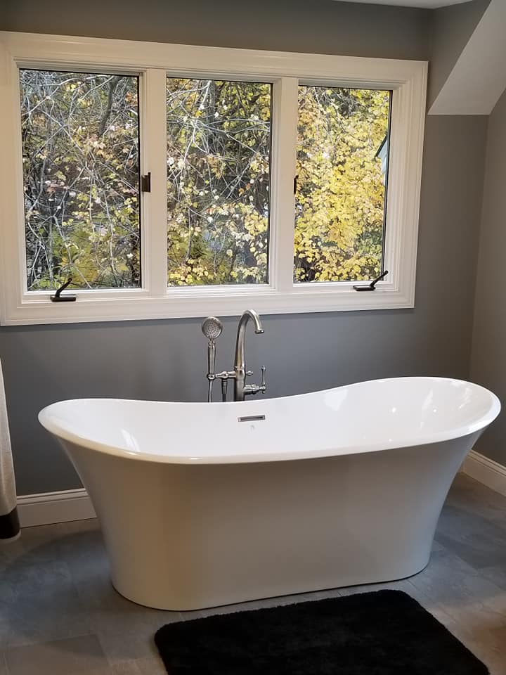 Freestanding white bathtub under large bathroom window